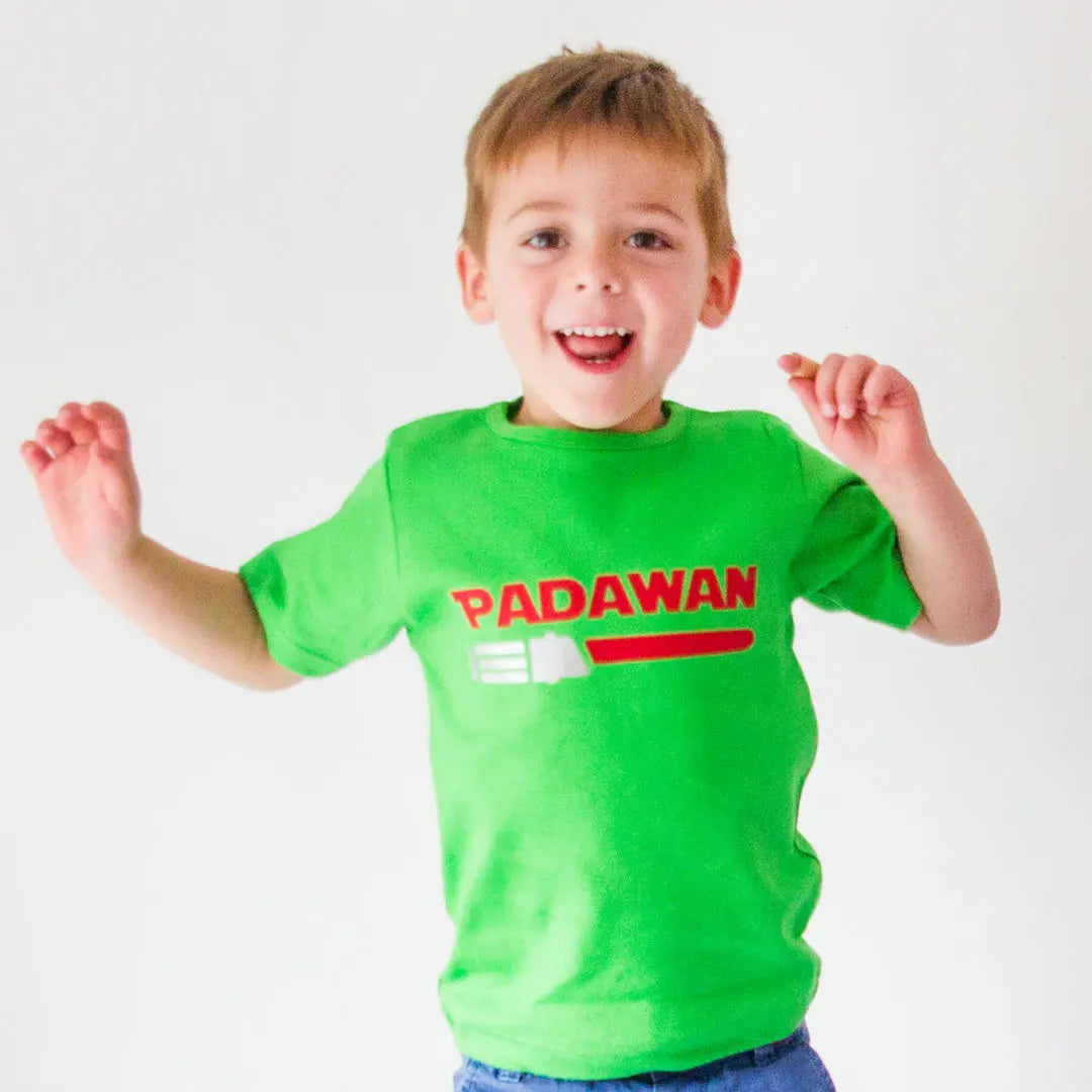 Boy wearing a green t shirt with the text Padawan and a red light saber with a silver handle underneath. The light saber can be changed to have different colour's, depending on whose side you are on!