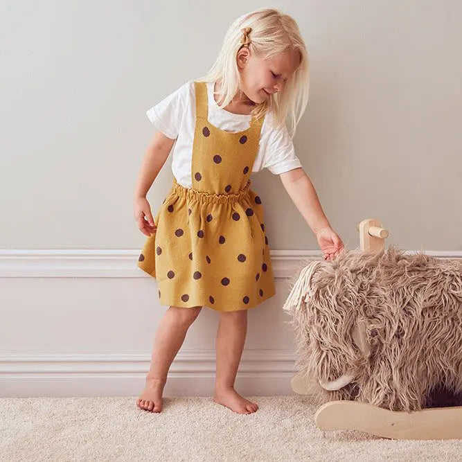 Girl standing next to a rocking mammoth toy, she is smiling and stroking the mammoth's head. It's a cream room, with a plush cream carpet.