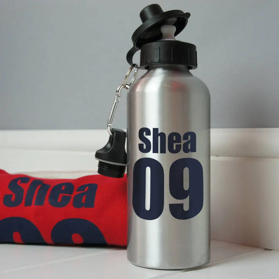 Silver aluminium water bottle printed with the name Shea 09, next to a red rugby shirt that also has the name Shea printed on it.