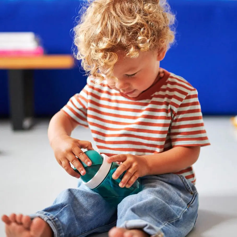 Toddler looking at his straw water cup. He is opening the lid.