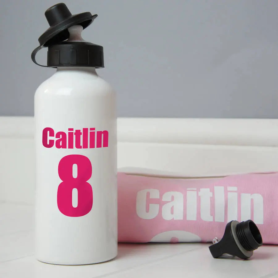White luminium water bottle with the name Caitlin and the number 8 printed on the bottle in pink. Next to the bottle is the second lid and a folded light pink rugby shirt with the name Caitlin on