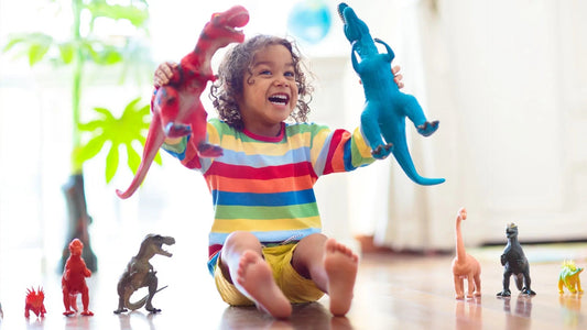 Child holding 2 large dinosaurs with many others around them. He wears a brightly striped jumper and looks like he is roaring