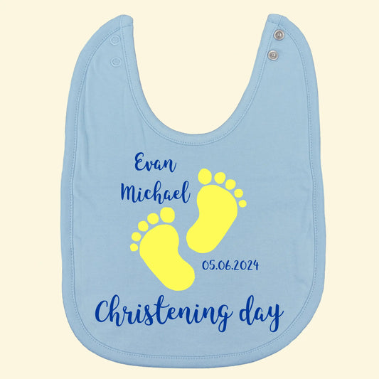 Light blue bib with christening design printed in royal blue and lemon yellow. Text reads Evan Michael. 05.06.2025, Christening day.