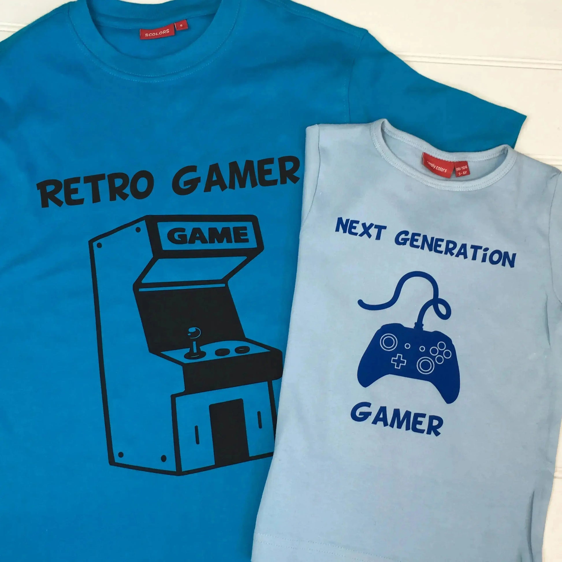 Adult t shirt with retro games console printed in black with Retro Gamer printed on top. Kids light blue t shirt with controller 1 printed in royal blue with two lines of text, top Next Generation, bottom line Gamer.