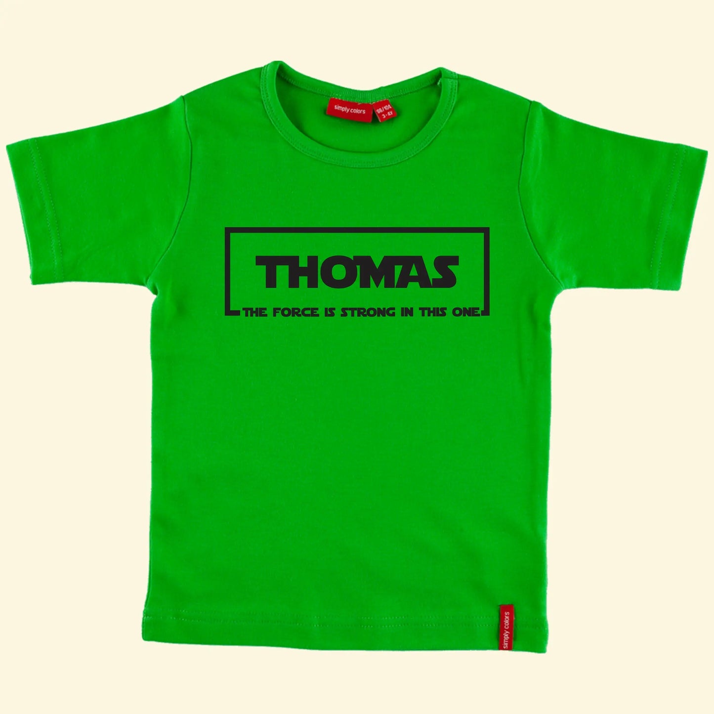 Kids green t shirt with the name Thomas printed in the middle of a rectangular box with The force if strong in this one at the bottom.