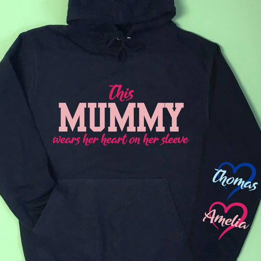 Adult navy hoodie, with This Mummy wears her heart on her sleeve printed on the front in two print colours. Down the right sleeve as photo (left hoodie when wearing) two hearts printed with child's names in the middle