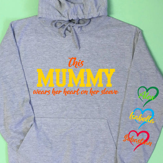 Adult grey hoodie, with This Mummy wears her heart on her sleeve printed on the front in two print colours. Down the right sleeve as photo (left hoodie when wearing) three hearts printed with child's names in the middle