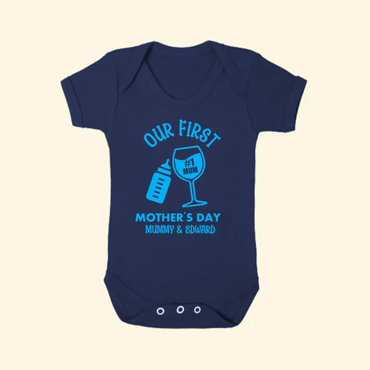 Navy babygrow with design of Our First Mother's Day Mummy & Edward. With a baby bottle and wine glass tilted together. Printed in blue.