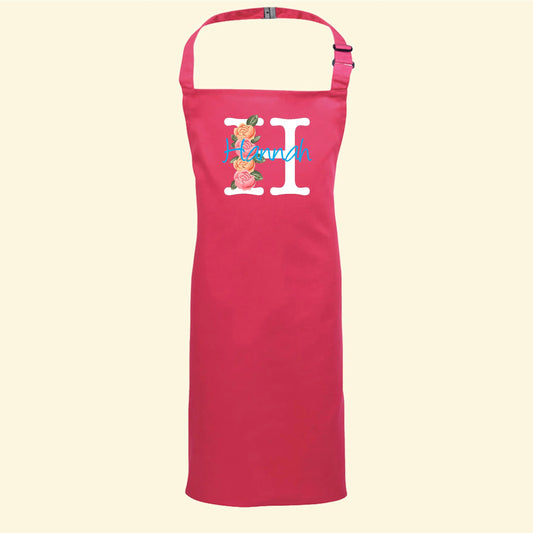 Pink apron with a monogram design. A capital H with roses along one side and the name Hannah written through the middle in a different font and colour