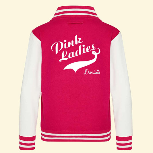 Kids pink varsity jacket with Pink Ladies text printed on a slight angle with a swoosh under the ladies text. Child's name printed below, all printed in white