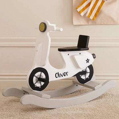 White personalised rocking scooter with the name Oliver printed in black. The scooter is in a beige room with plush carpet.