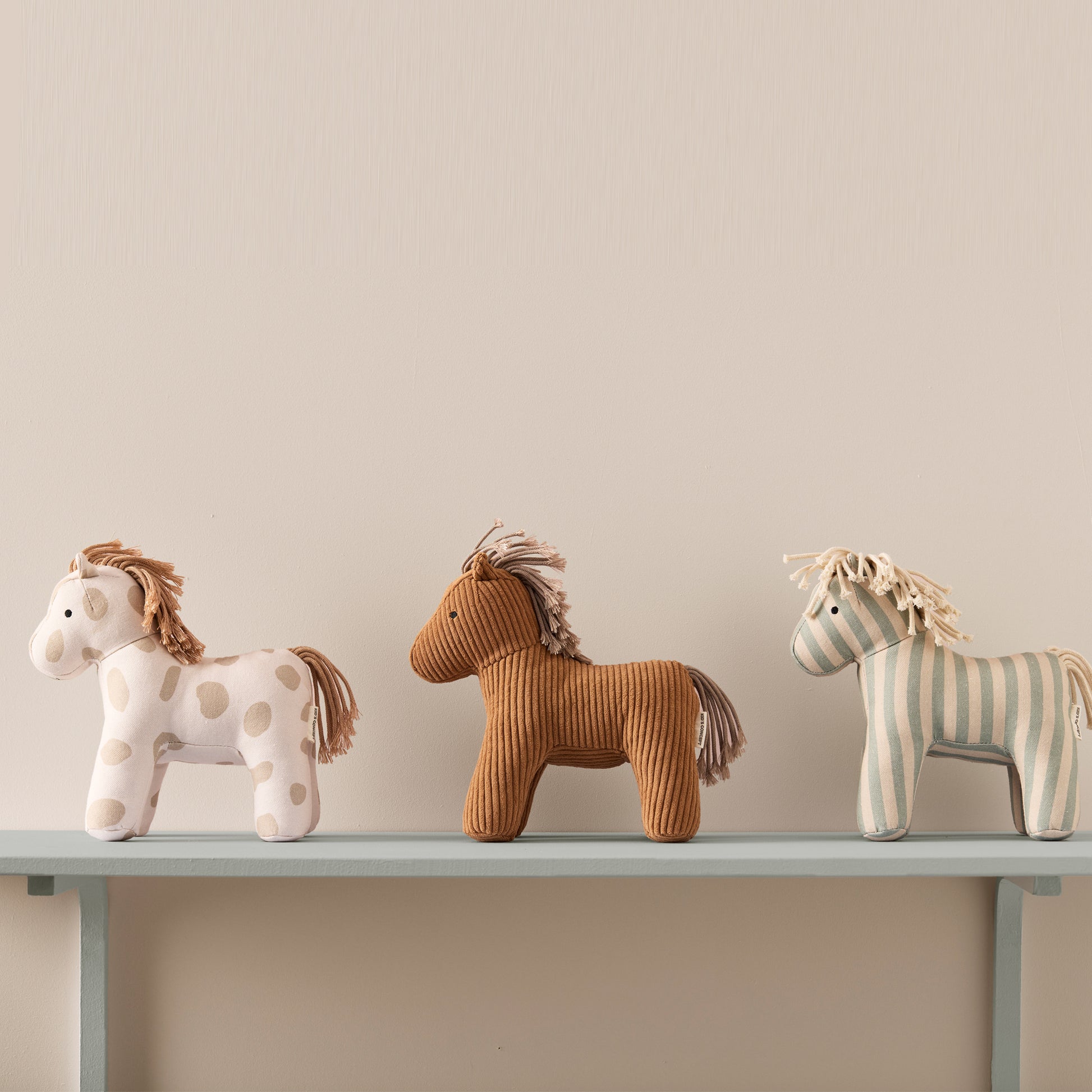 Three cute horse toys in a line. Left side Dotty:  playful polka dots material, middle Vera: soft brown ribbed material, right side Sam: white and light blue stripped material.