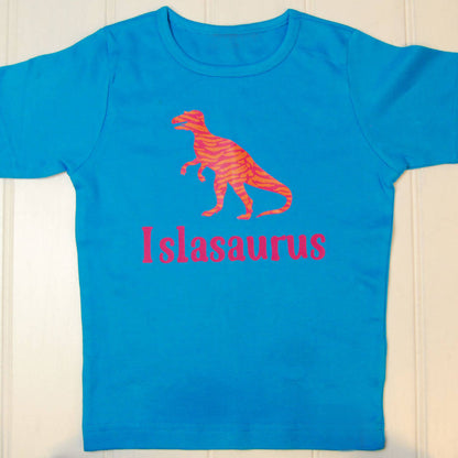 Aqua blue t shirt with an orange and pink striped t rex and the name Islasaurus printed on the front in pink