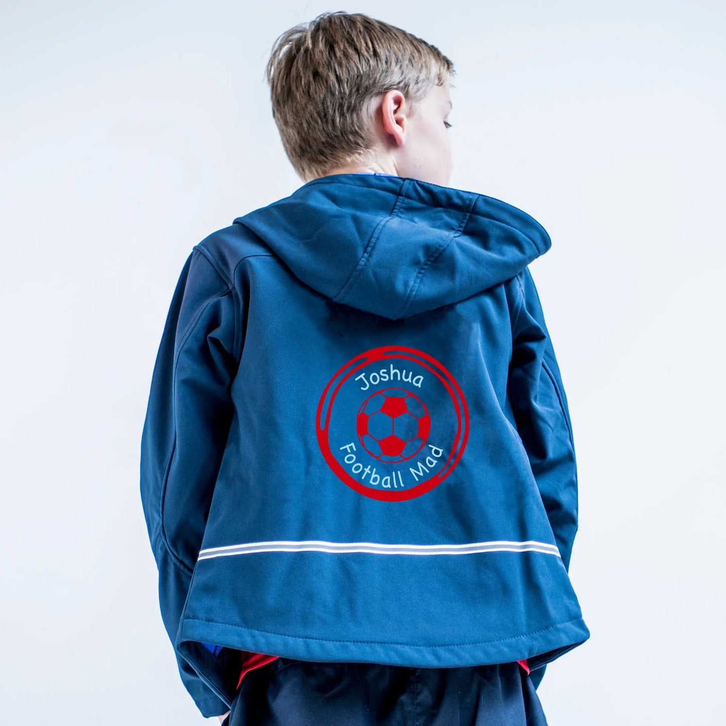 Boy wearing a blue softshell jacket, with a football design on the back. The football and surround is red, inside the surround is the name Joshua above the football and Football mad underneath the ball in light blue print. 