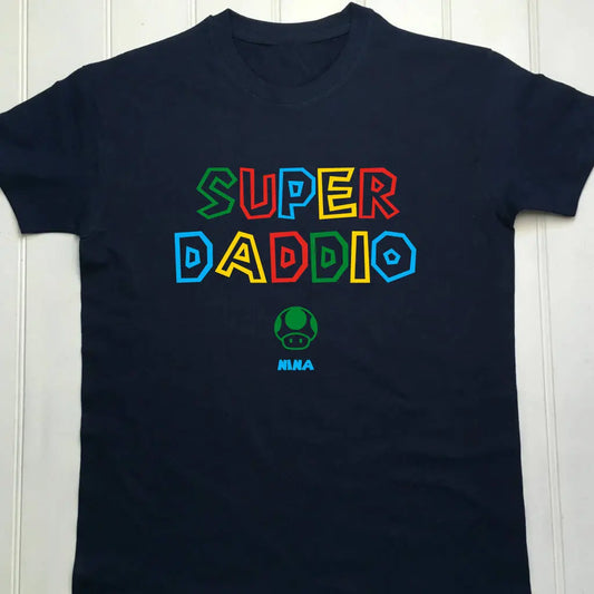 Navy adult's t shirt with a colourful Super Daddio design, a play on the super Mario game. Underneath is a green mushroom with the name Nina printed in blue. The number of mushrooms can change depending on the number of children the parent has.