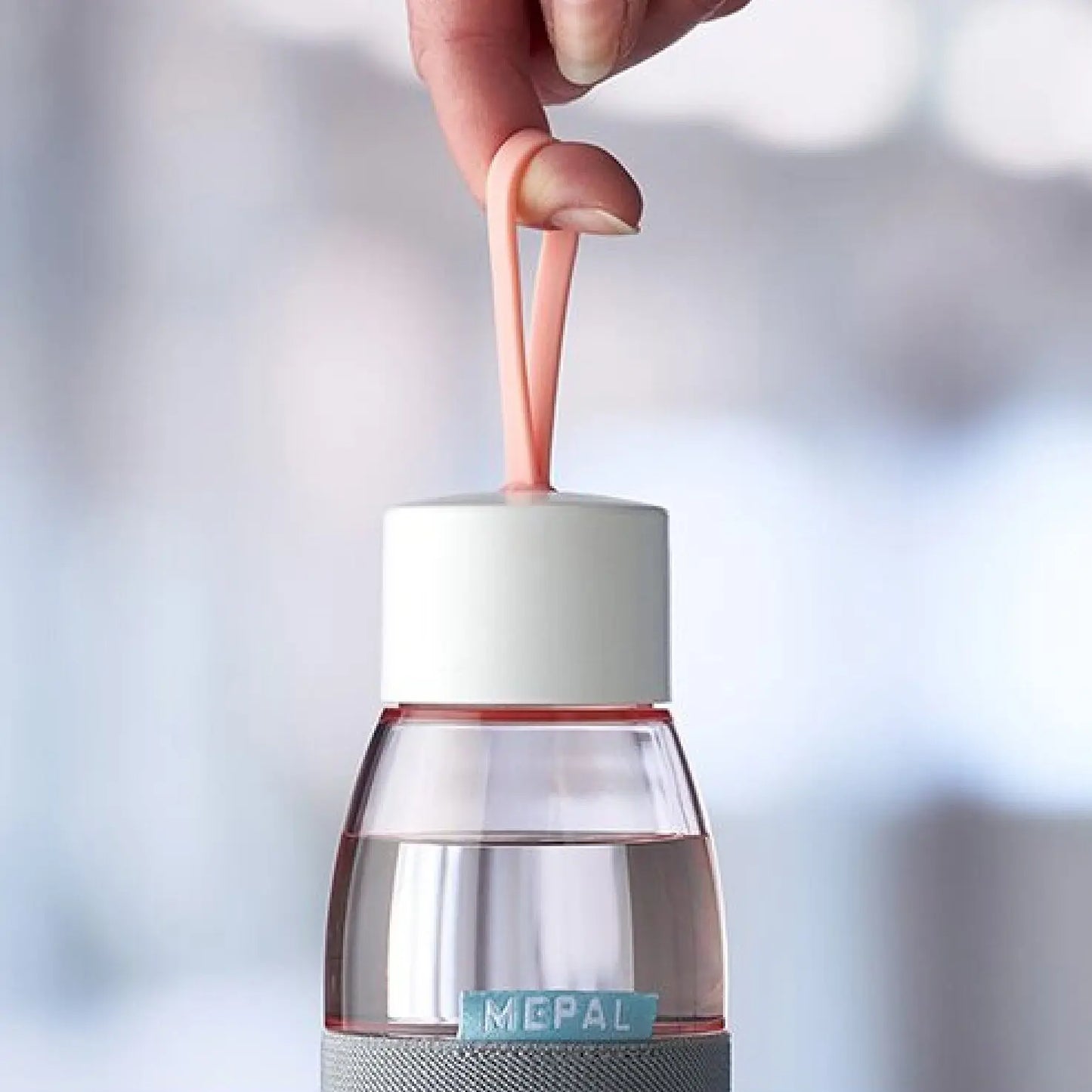 Close up of a nordic pink ellipse water bottle by mepal, being held with a finger by the loop on the lid