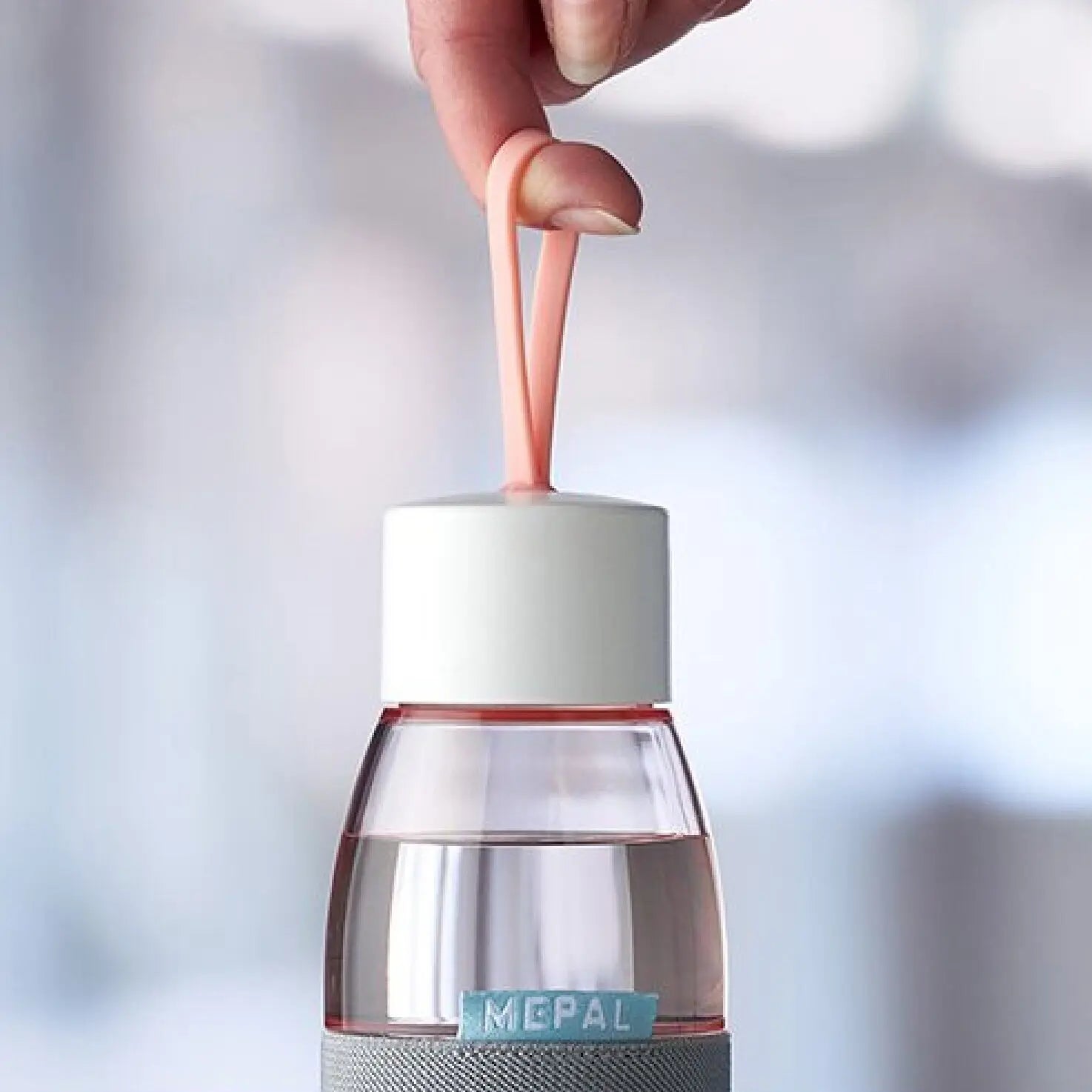 Close up of a nordic pink ellipse water bottle by mepal, being held with a finger by the loop on the lid