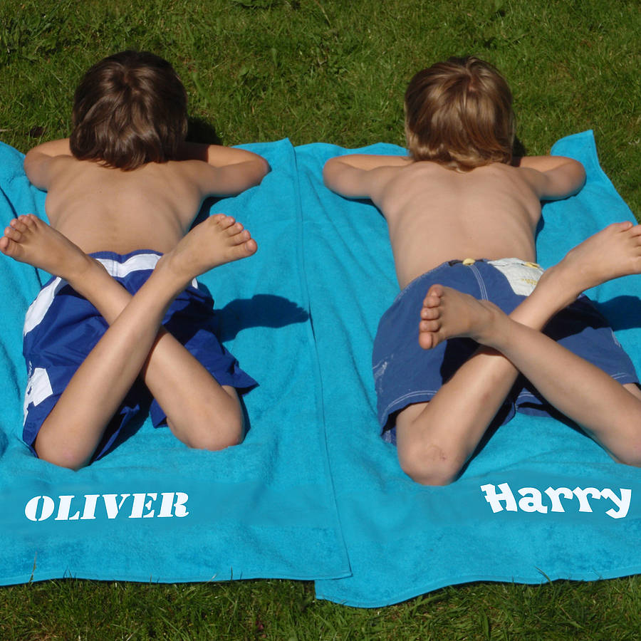 Two boys laying on beach towels that have their names printed on them