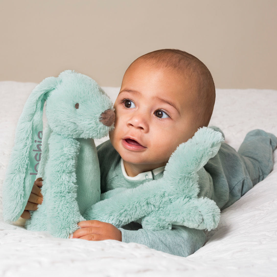 Baby holding a seagreen rabbit soft toy, with their name embroidered on the ear