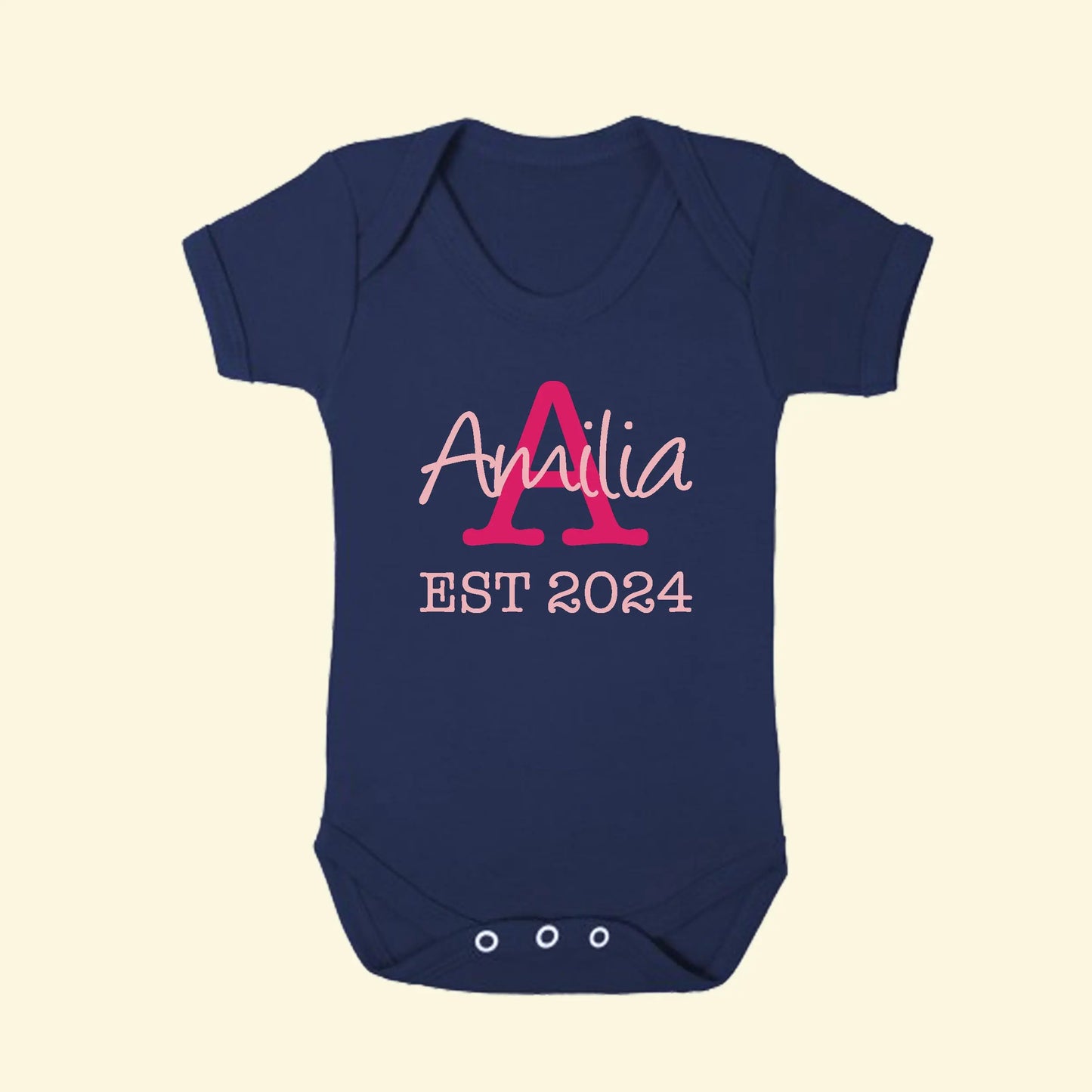 Navy blue babygrow with a capital A in fuchsia pink and the name Amilia printed across the A in light pink, with EST 2024 in light pink underneath.