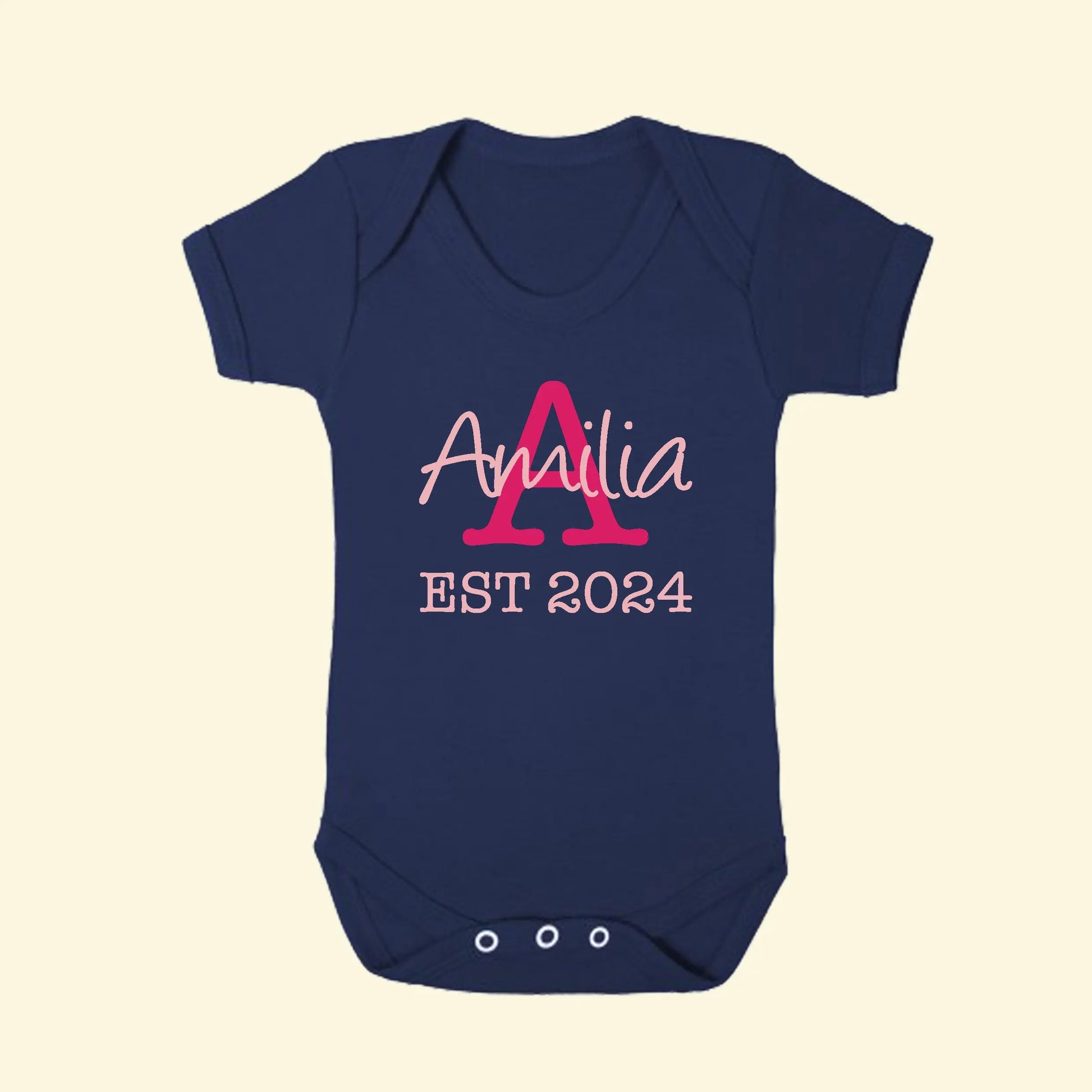 Navy blue babygrow with a capital A in fuchsia pink and the name Amilia printed across the A in light pink, with EST 2024 in light pink underneath.