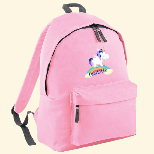 Light pink backpack with a unicorn sitting on a rainbow and the name Charlotte printed on the front