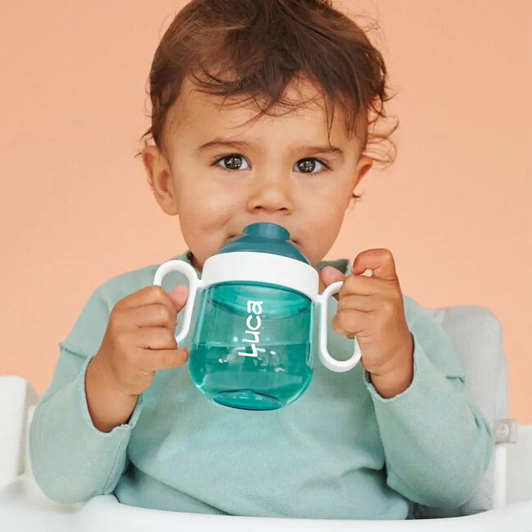 Toddler holding a turquoise sippy cup, with his name Luca printed on the cup