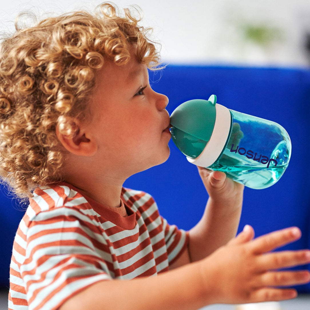 A toddler drinking from a turquoise straw cup with the name Jenson printed on the cup in navy blue