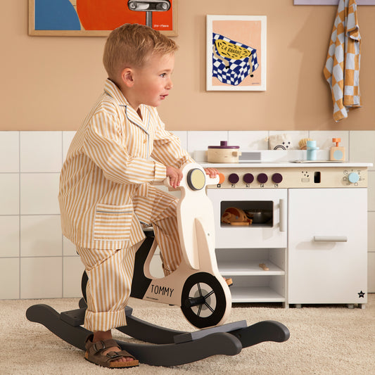 A little boy playing on a personalised rocking scooter toy, with the name Tommy printed on the scooter.