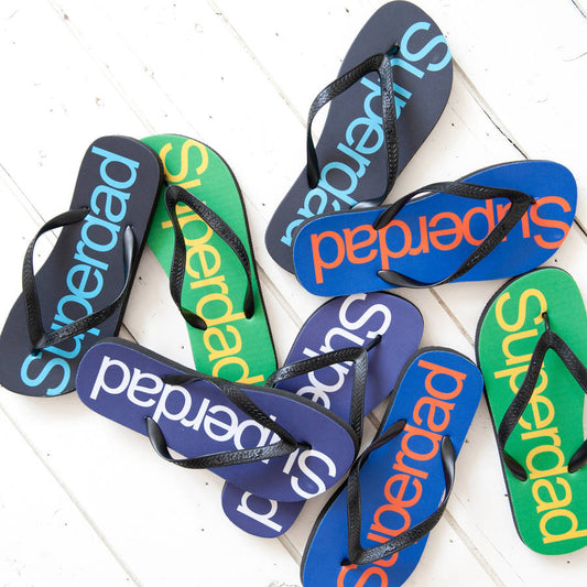 A variety of flip flops all with Superdad printed on the centre of the flip flop in various colour combinations