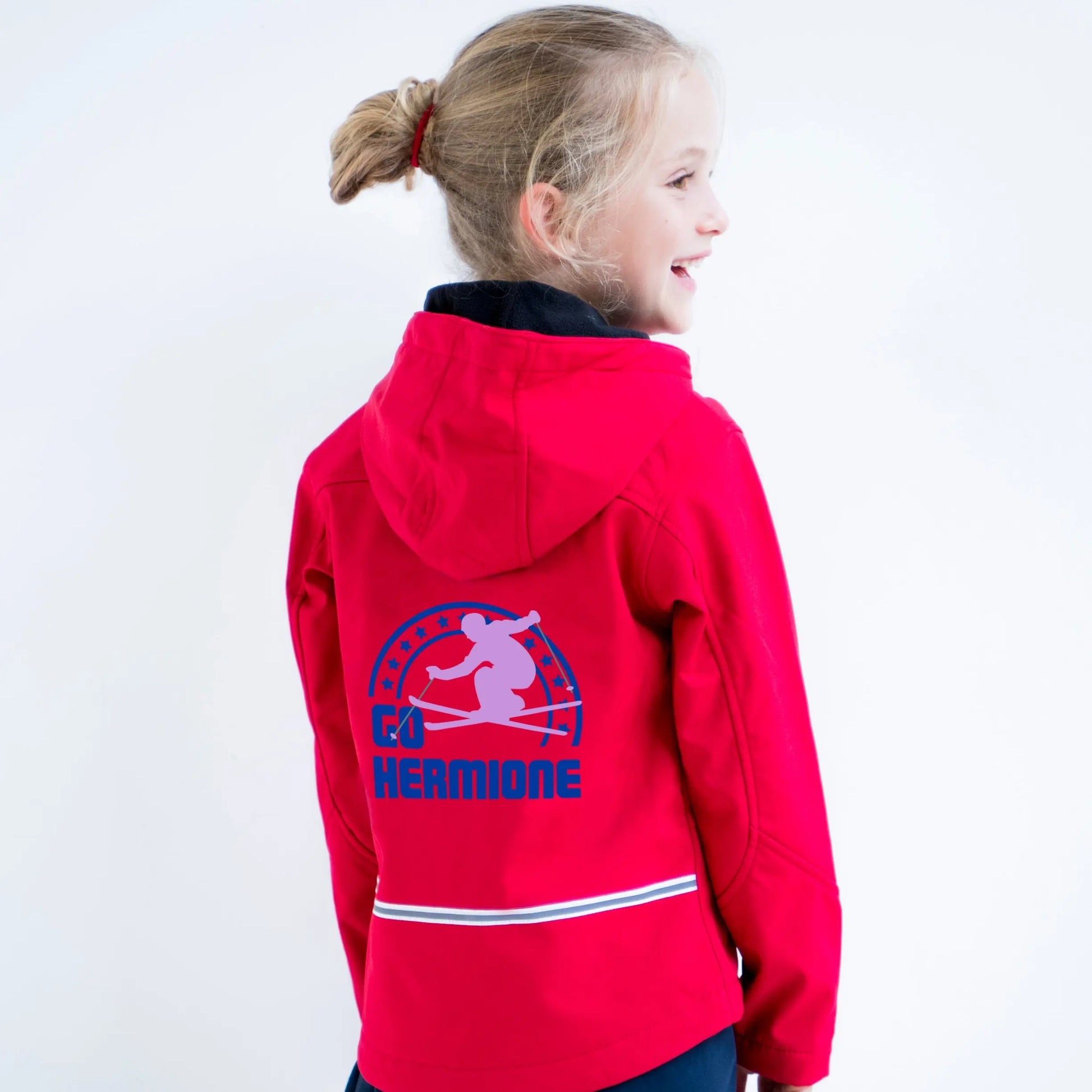 Girl wearing a red soft shell jacket with a ski design on the back with the text Go Hermione printed in royal blue and lilac
