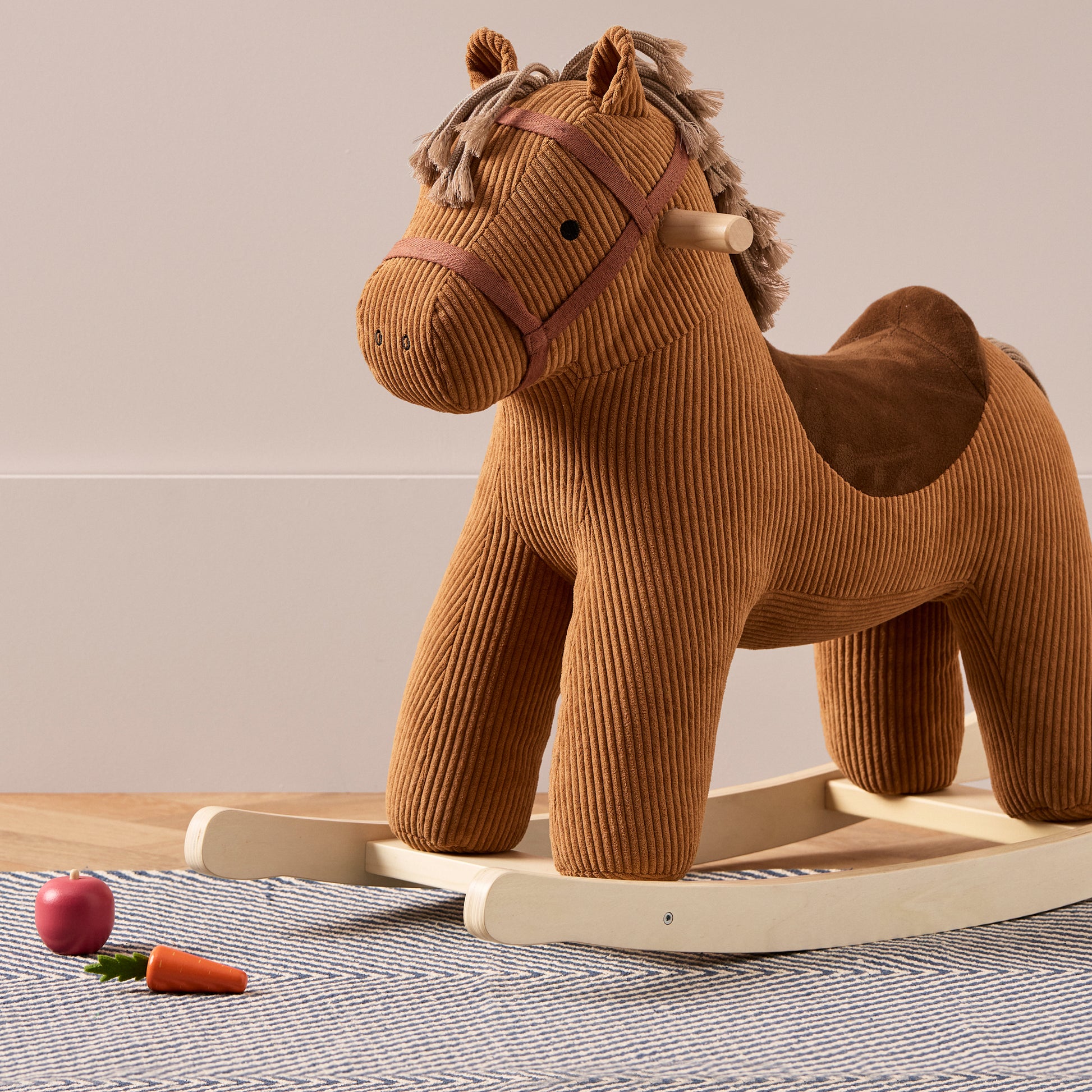 Rocking horse Vera toy with a toy apple and carrot on the floor by the rockers